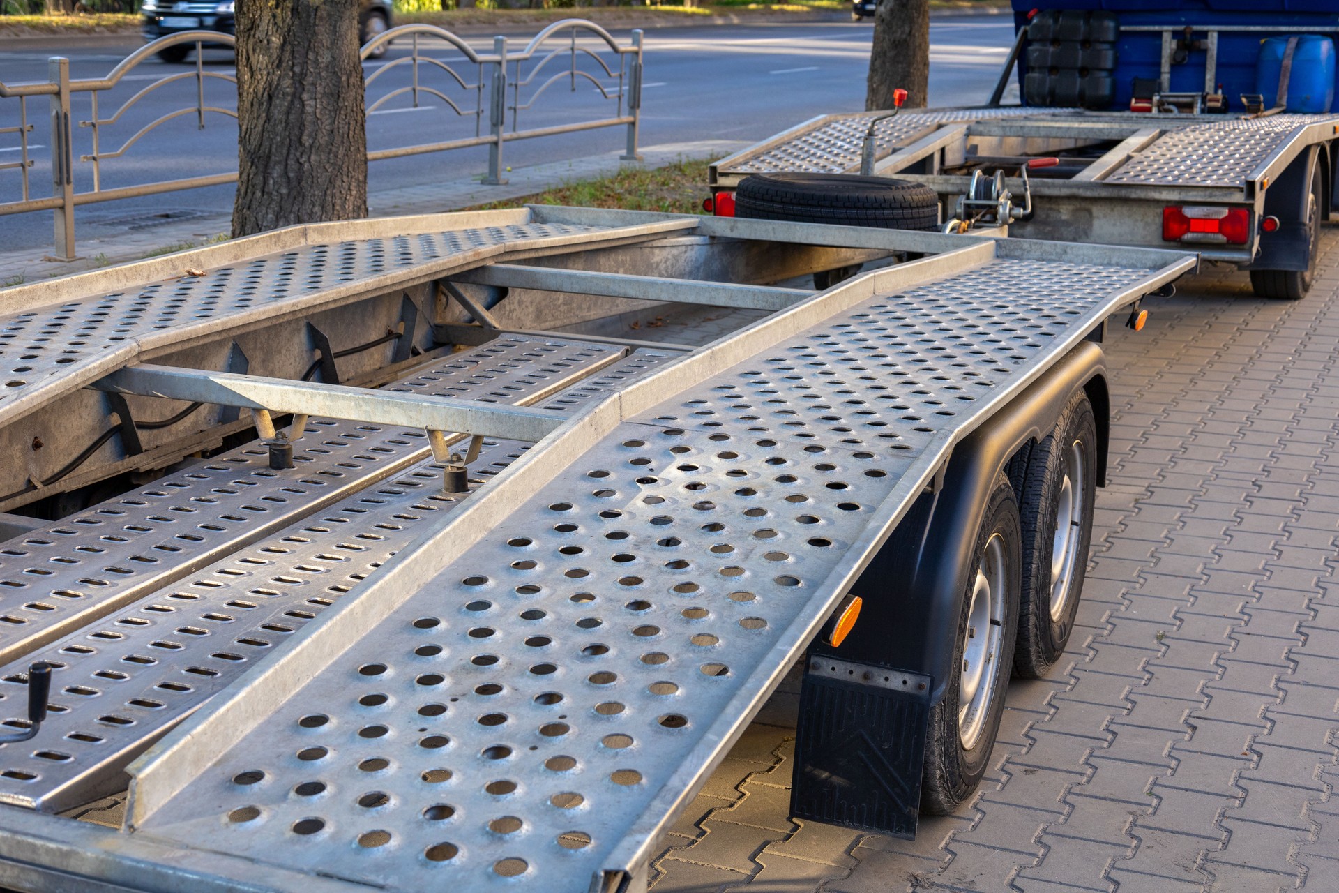 A trailer sits beside the road, displaying metal construction with a perforated surface and a sturdy build during a sunny day