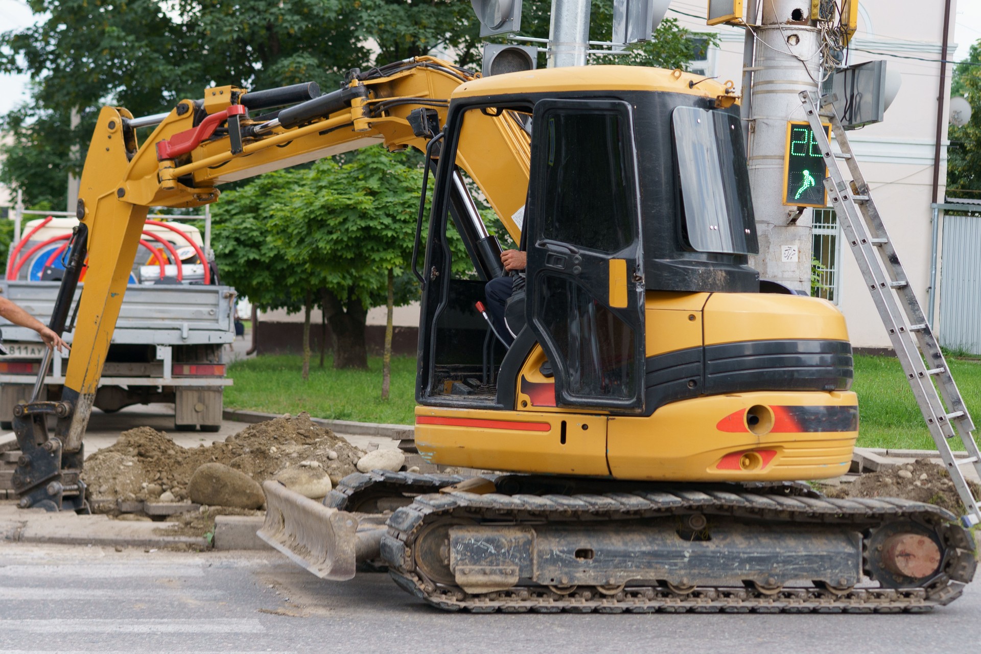 Construction worker operates yellow excavator on city street during road maintenance work