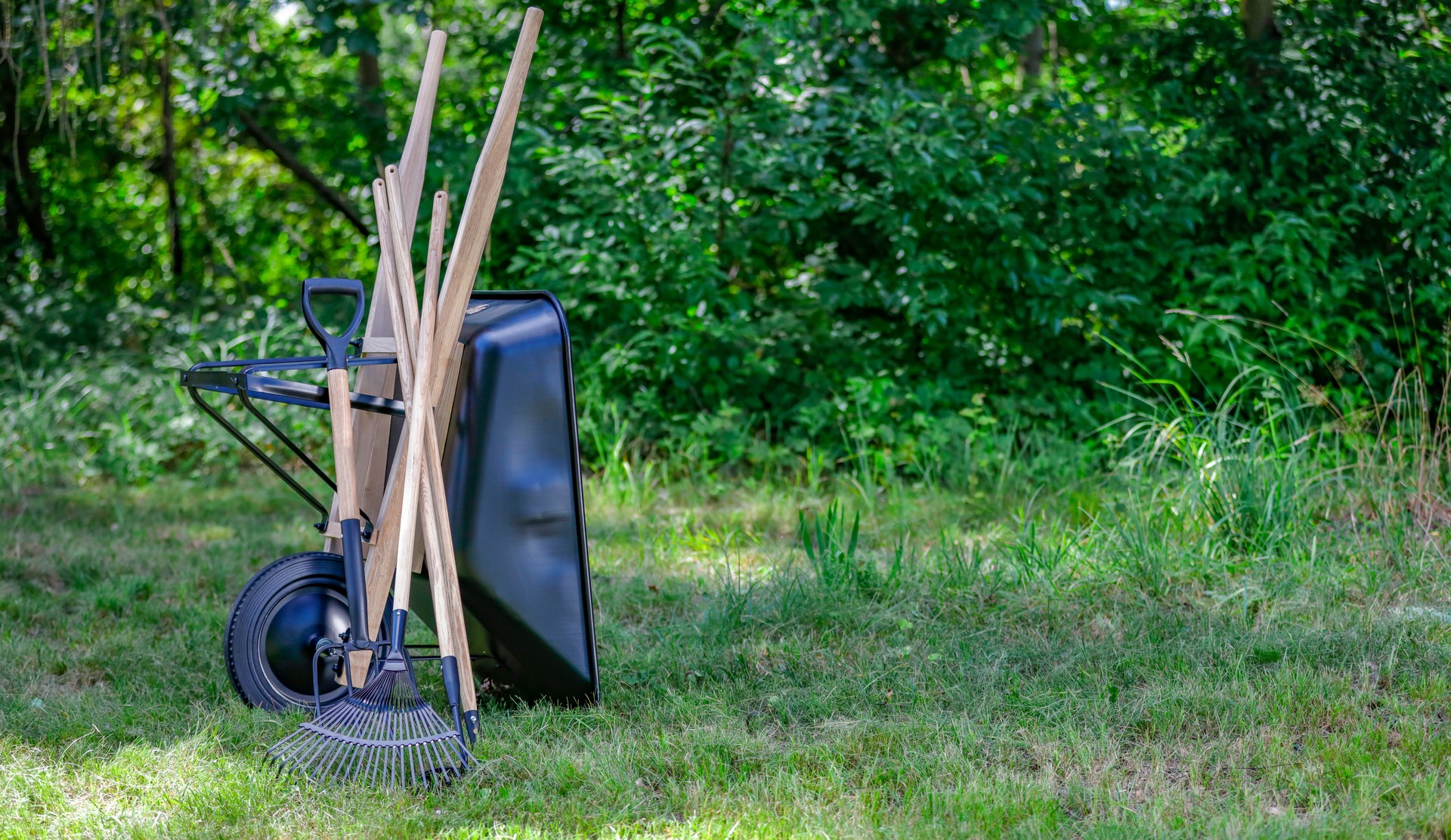 Garden tools and wheelbarrow on grassy lawn with green background of garden or park setting. Outdoor work and gardening.