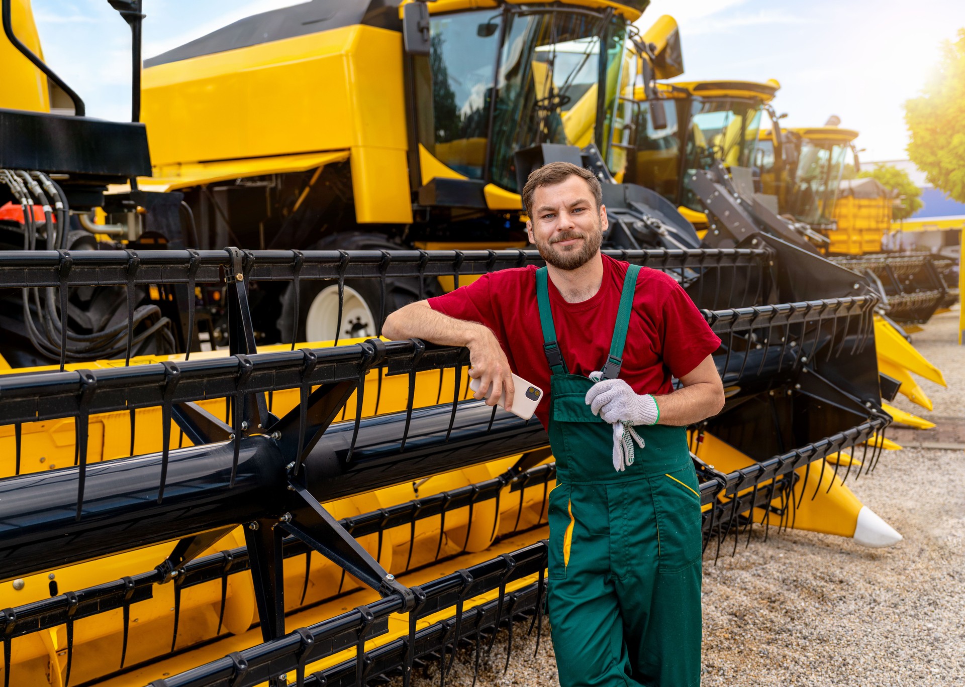 Male agricultural technician by combine harvester at equipment yard or dealership